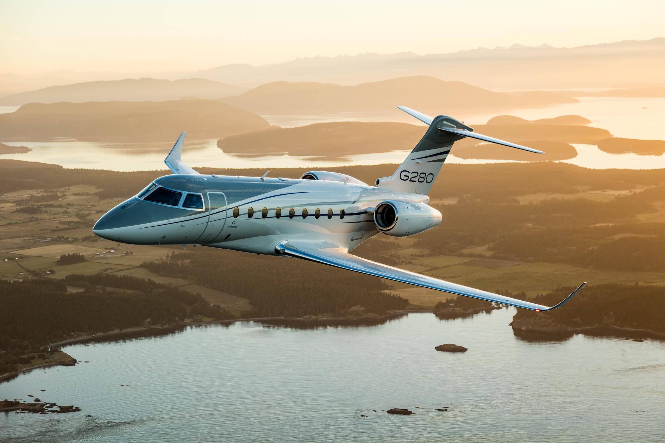 G280 aircraft flying above land and water at sunset