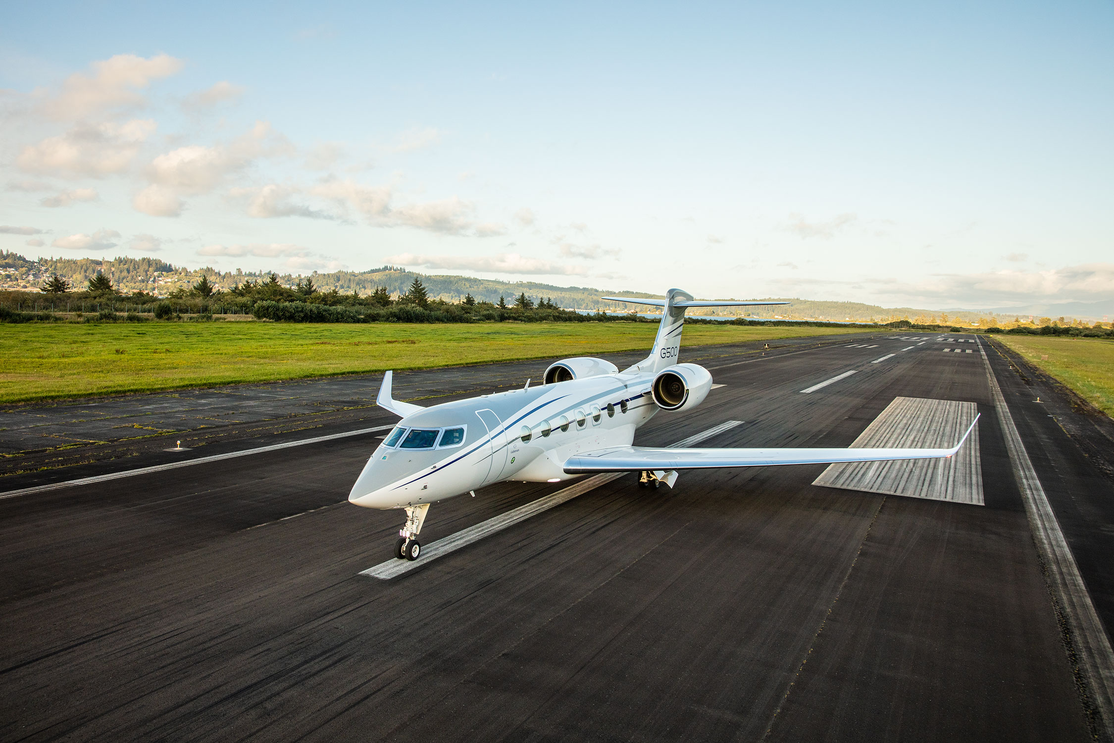 G500 aircraft parked on runway with green fields and trees in the distance