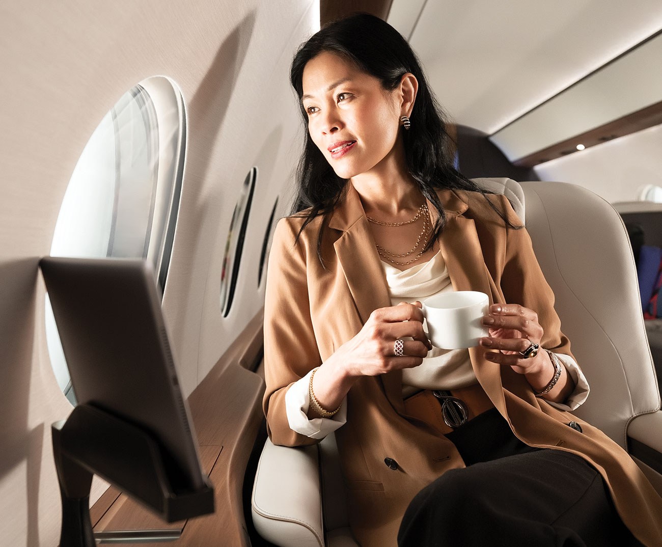 Women enjoys hot beverage in leather chair while gazing out aircraft window